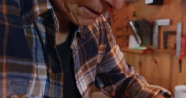 Kafkasyalı bir kadın Luthier 'in atölyesinde yarım kalmış bir kemanla çalışırken, vücudu bıçakla şekillendirirken yan görüntüsü.