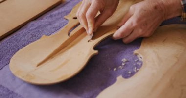 Atölyesinde bir keman tezgahında keman üzerinde çalışan beyaz bir kadın Luthier 'in ellerini kapatın. Keskin bir bıçakla kemanın ön panelinin içini şekillendirin..