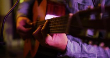 Bir kayıt stüdyosunda akustik gitar çalan beyaz bir erkek gitaristin yan görüntüsü. Müzisyenler bir şarkı üzerinde çalışıyor.