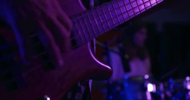 Kayıt stüdyosunda pembe ışık altında bas gitar çalan bir adamın ön görüntüsü. Arka planda uzun saçlı, beyaz bir erkek davulcu var. Müzisyenler bir şarkı üzerinde çalışıyor.