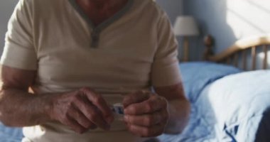 Üst düzey beyaz bir adamın yatak odasında ön tarafta oturması, her sabah kalktıktan sonra bir hap kutusundan tablet alması, ağır çekim.