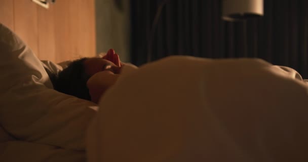 夜にベッドに横になって腕を伸ばして オフ時間を楽しんでリラックスした若い白人女性の側面図 — ストック動画