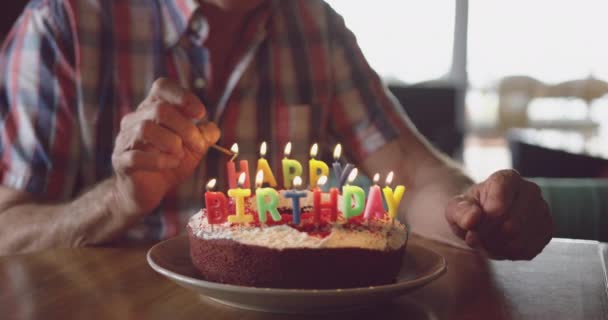 一个白人老人坐在餐桌旁 点燃生日蛋糕上的蜡烛 脸上挂着火柴 笑容满面 动作缓慢 — 图库视频影像