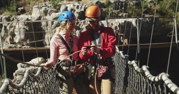 画面中 年轻的白种人夫妇穿着拉链衬里的设备 男人在阳光明媚的山中使用智能手机 动作缓慢 在南非的冒险假期 — 图库视频影像