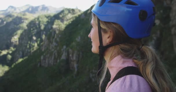 ヘルメットをかぶった若い幸せな白人女性の肖像画を眺めながら 山の中で晴れた日にジップライン スローモーションを賞賛 南アフリカでのアドベンチャーバケーション — ストック動画