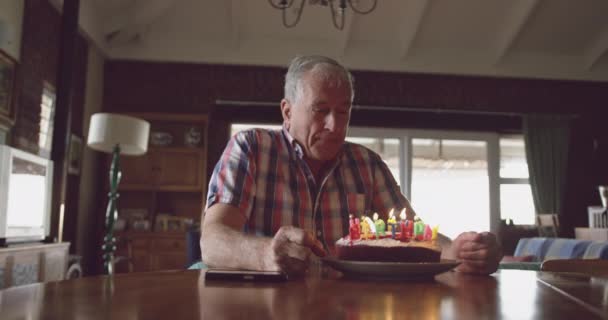 一个白人老人独自坐在餐桌前 在面前吹灭生日蛋糕上的所有蜡烛 笑容满面 动作缓慢 — 图库视频影像