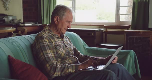 一个白人老人在客厅里悠闲自在地坐在沙发上 用笔记本电脑 慢动作的侧视图 — 图库视频影像