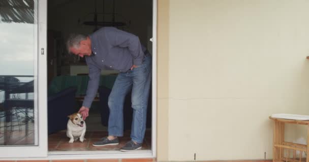 一个年长的白人男子在家里放松下来 站在敞开的门口弯下腰去摸他的宠物狗 慢动作的侧视图 — 图库视频影像