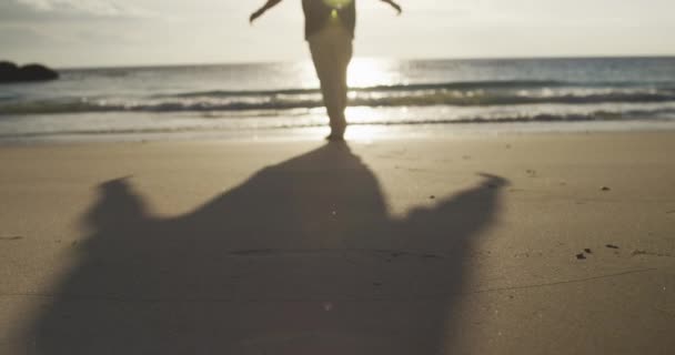 一个年长的白人男子面对着日落时张开的双臂 慢吞吞地在海滩上独自行走的后视镜 — 图库视频影像