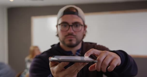 一个白种人在一个创意十足的办公室里工作 戴着帽子和眼镜 拿着平板电脑 看着相机 慢动作 — 图库视频影像