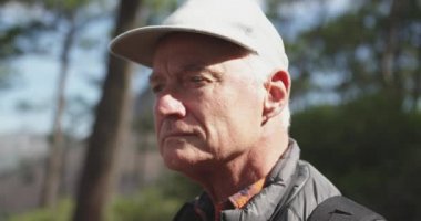 Side view of a senior Caucasian man enjoying time in nature, wearing a hat standing in forest during a hike, slow motion