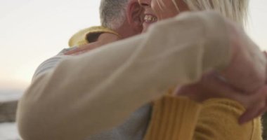 Side view close up of a senior Caucasian couple enjoying time in nature together, dancing on a beach at sunset, smiling, slow motion