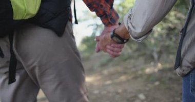Rear view mid section of a senior Caucasian couple enjoying time in nature together, walking with backpacks, holding hands, hiking in mountains, slow motion