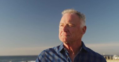 Side view of a happy senior Caucasian man enjoying time in nature, admiring the view, standing by the sea on a sunny day, slow motion