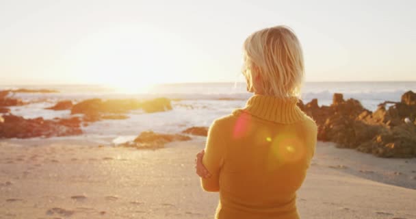 自然の中で時間を楽しんで幸せなシニア白人女性のサイドビュー 笑顔と夕日を賞賛 ビーチで海のそばに立って スローモーション — ストック動画