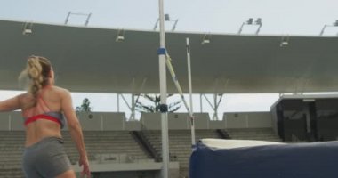 Side view of a Caucasian female athlete practicing at a sports stadium, doing high jump jumping over the bar, slow motion