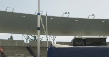 Beyazlı bir erkek sporcunun spor stadyumunda antrenman yaparken, yüksek atlama yaparken bardan düşerken, ağır çekimde...