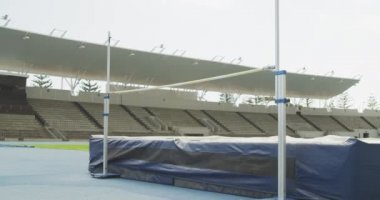 Spor stadyumunda antrenman yapan, barın üzerinden atlayan, ağır çekimde zıplayan melez bir erkek sporcunun yan görüntüsü.