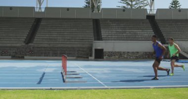 Kafkas ve karışık ırk erkek sporcularının spor stadyumunda antrenman yaparken, ağır çekimde birbirleriyle yarışırken yan görünümü.