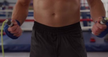 Front view mid section of a mixed race male boxer holding a skipping rope in a boxing gym, slow motion