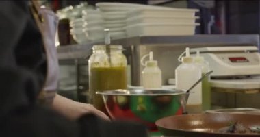 Kafkasyalı bir aşçının yan görüntüsü yoğun bir restoranda çalışıyor, taze soğan dilimliyor, tabaklar kesme tahtasının yanında hazır.