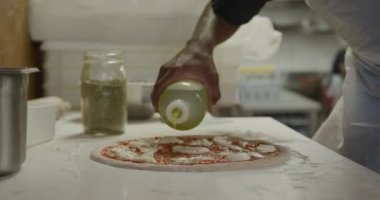 Yoğun bir pizza restoranında çalışan melez bir aşçının elini kapatıyoruz. Pişirmeden önce pizza hamurunun üzerine yağ döküyoruz.