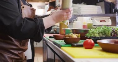 Yoğun bir restoranda çalışan beyaz bir kadın aşçının yan görüntüsü patates salatası süslerken arka planda çalışan erkek arkadaşı.