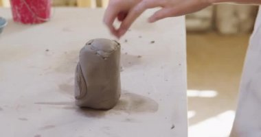 Kafkasyalı genç bir çömlekçinin orta kesiminde önlük takmış vaziyette bir çömlek atölyesindeki bir kabloyla kilden bir parçayı kesiyor.