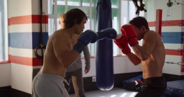 Front view of a bald Caucasian male instructor during boxing training in a boxing gym instructing two male boxers, slow motion