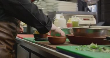 Yoğun bir restoranda çalışan beyaz bir kadın aşçının yan görüntüsü, limon suyuyla patates salatası süslerken, arka planda çalışan meslektaşları...