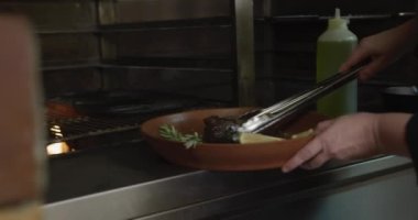 Meşgul bir lokanta mutfağında çalışan, ızgaranın içine et koyan, alevlerin üzerine yağ döken beyaz bir kadın aşçının ellerini kapatın.