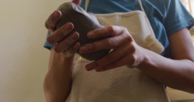 Kafkasyalı genç bir çömlekçinin ön tarafı. Önlük takıyor, elinde bir parça kil tutuyor ve elleriyle çömlek atölyesinde şekilleniyor.