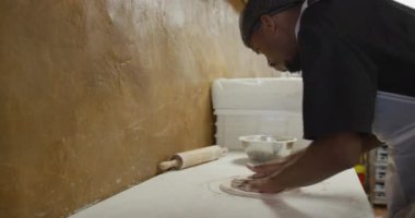 Side view of a mixed race male cook working in a busy pizza restaurant kitchen, preparing pizza dough before cooking
