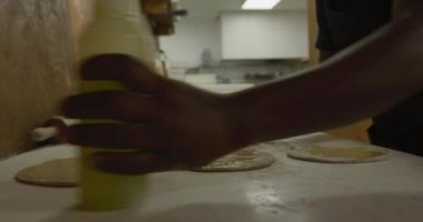 Meşgul bir pizza restoranında çalışan, pizza hamurunu yağlayan ve pizza kabuğuyla pizza fırınına koyan Afro-Amerikalı bir aşçının yan görüntüsü.