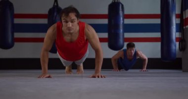 Front view of a mixed race male boxer and a Caucasian male boxer doing push ups in a boxing gym, slow motion