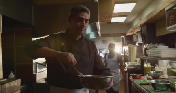 忙しいレストランのキッチンで働く白人男性シェフの正面図 背景で働くボウル 男性と女性の料理人を混ぜます — ストック動画