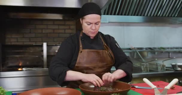 一个白人女厨师在一个繁忙的餐馆厨房里工作 装饰和准备牛排 后面是炉火熊熊熊燃烧的场景 — 图库视频影像