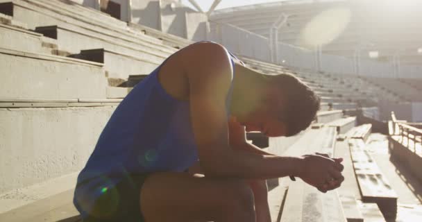 競技の前に座って集中し 遅い動き 空のスポーツスタジアムでの混合レースの男性選手の側面図 — ストック動画