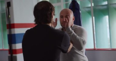 Krav Maga Training. Front view of a bald Caucasian male instructor giving self defence training in a boxing gym to a mixed race man, slow motion