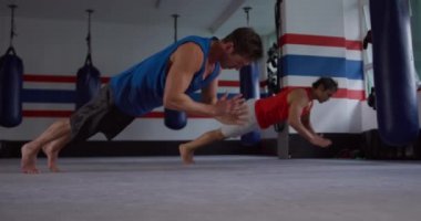 Side view of a Caucasian male boxer and a mixed race male boxer doing push ups in a boxing gym, slow motion