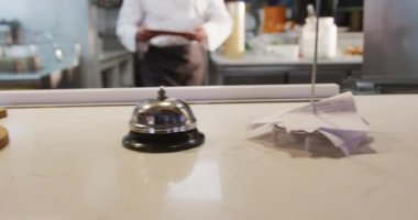 Yoğun bir lokanta mutfağında çalışan beyaz bir aşçının orta bölümü sipariş istasyonuna servis edilecek bir tabak getiriyor.