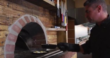 Yoğun bir pizza restoranında çalışan beyaz bir aşçının yan görüntüsü pizza fırınına tabak koyması arka planda çalışan kadın aşçı...