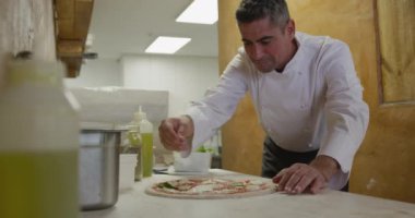 Side view mid section of a Caucasian male chef working in a busy pizza restaurant kitchen, preparing pizza before cooking