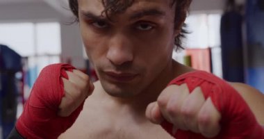 Portrait close up of a young mixed race male boxer with his hands wrapped in boxing bands looking at camera in a boxing gym, slow motion