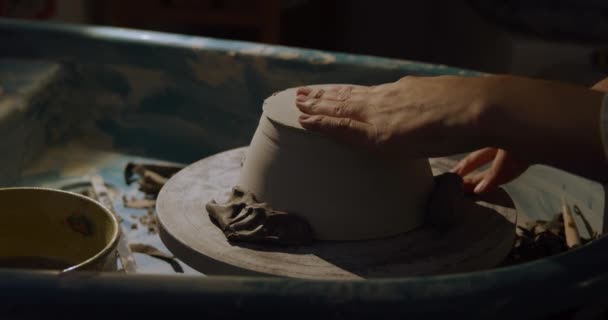 若い白人女性の陶芸家がろくろで土皿を回し 陶器の工房で道具で形を作る様子を横に見る — ストック動画