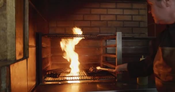 Vue latérale d'une cuisinière caucasienne travaillant dans une cuisine de restaurant occupée, cuisinant de la viande à l'intérieur du gril, versant de l'huile sur les flammes 