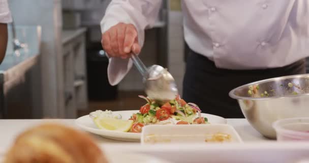 忙しいレストランのキッチンで働く白人男性シェフのフロントビューの中央部 提供される料理のプレートを飾る 彼の隣で働く女性料理 — ストック動画