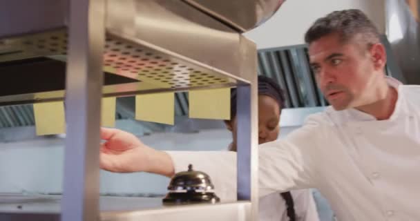 忙しいレストランのキッチンで働く白人男性シェフの正面図 彼の隣で働くアフリカ系アメリカ人女性料理人の注文をチェックする — ストック動画