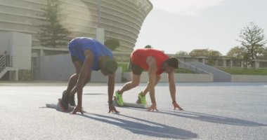 Bir spor stadyumunda antrenman yapan beyaz ve karışık ırktan erkek sporcuların yan görüntüsü. Koşu bloklarından, ağır çekimde koşmaya başlıyorlar.