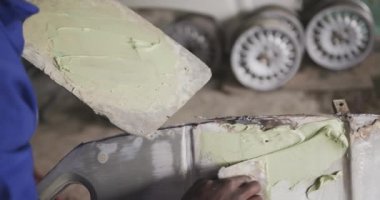 Kasabada bir panelci atölyesinin sahibi Afrikalı bir erkek, çalışanının yanında duruyor, bir araba parçasını boyuyor, talimatlar veriyor, yavaş çekim.
